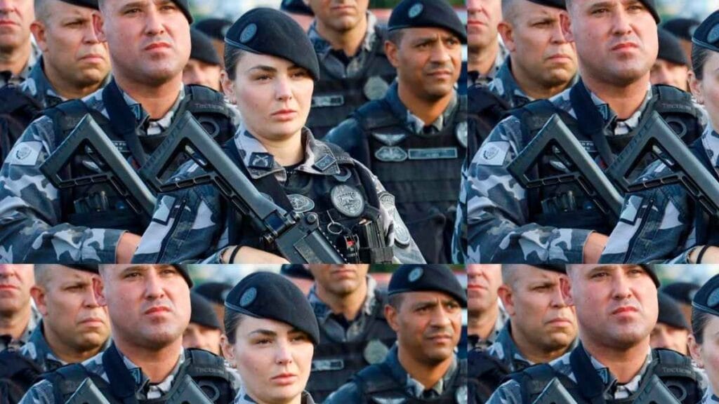 Grupo de policiais militares fardados, incluindo uma policial mulher ao centro, posam em formação com fuzis cruzados e expressão séria durante solenidade