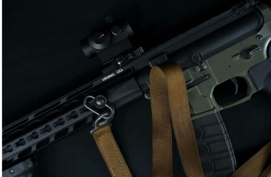 Imagem mostra um fuzil preto e verde-oliva com alça tática marrom, visor óptico e detalhes metálicos. O fundo escuro destaca o armamento.