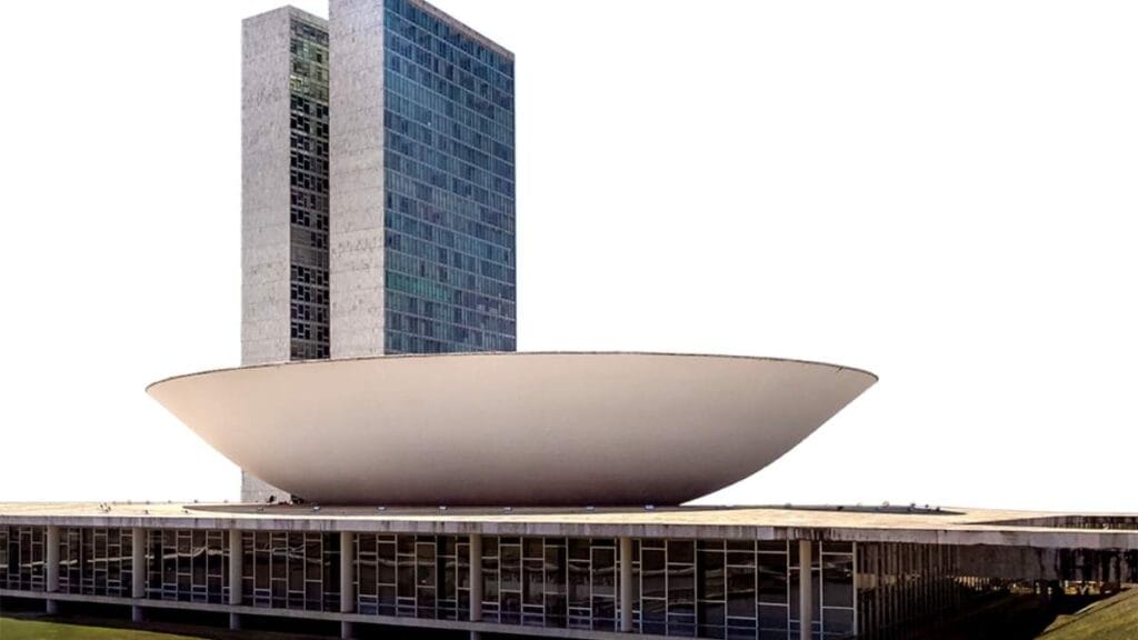Foto da fachada do Congresso Nacional, em Brasília, com destaque para a cúpula voltada para cima, que representa a Câmara dos Deputados, e as torres laterais. O céu está limpo ao fundo.