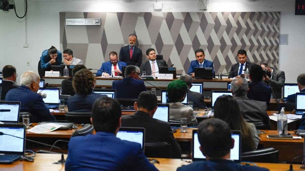 Sessão da Comissão de Constituição e Justiça do Senado Federal com parlamentares reunidos em plenário; senadores utilizam notebooks e participam de debate sobre projetos legislativos. Na mesa principal, membros da comissão acompanham a pauta com atenção.