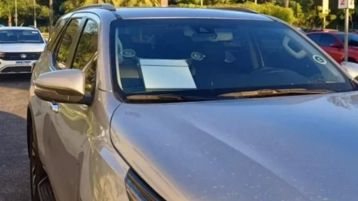PRF: Veículo SUV de cor prata está estacionado em local público durante o dia, com um starlink apoiado no painel frontal, visível pelo para-brisa. Equipamento está fixado com ventosas no vidro dianteiro. Ao fundo, outros veículos estão estacionados.