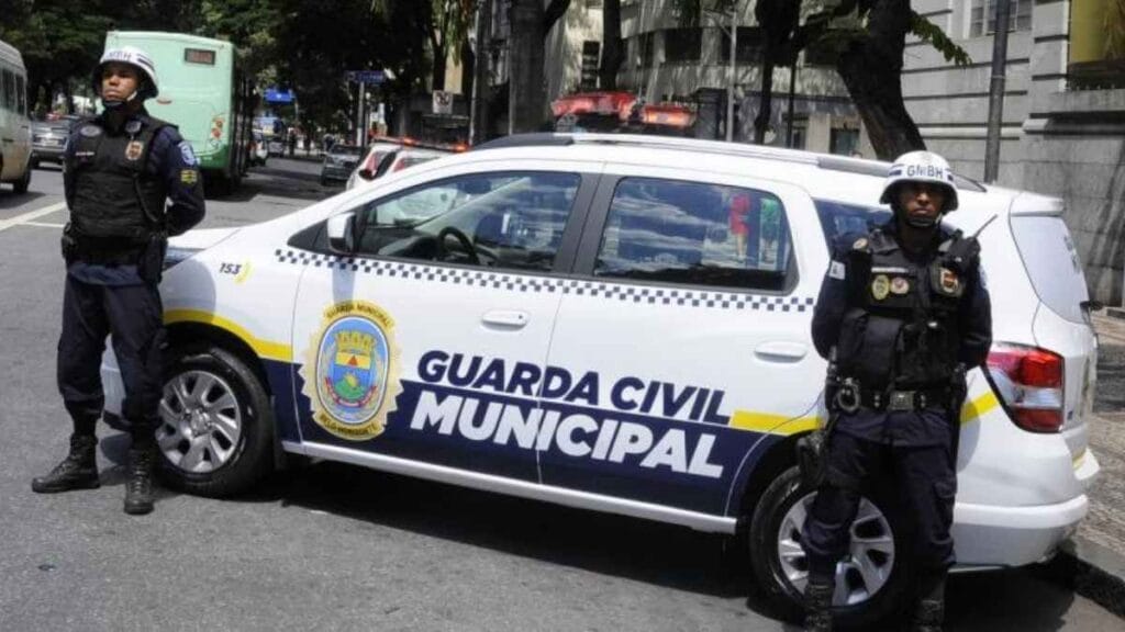 Dois guardas civis municipais de Belo Horizonte posicionados ao lado de uma viatura oficial, em patrulhamento urbano no centro da cidade.