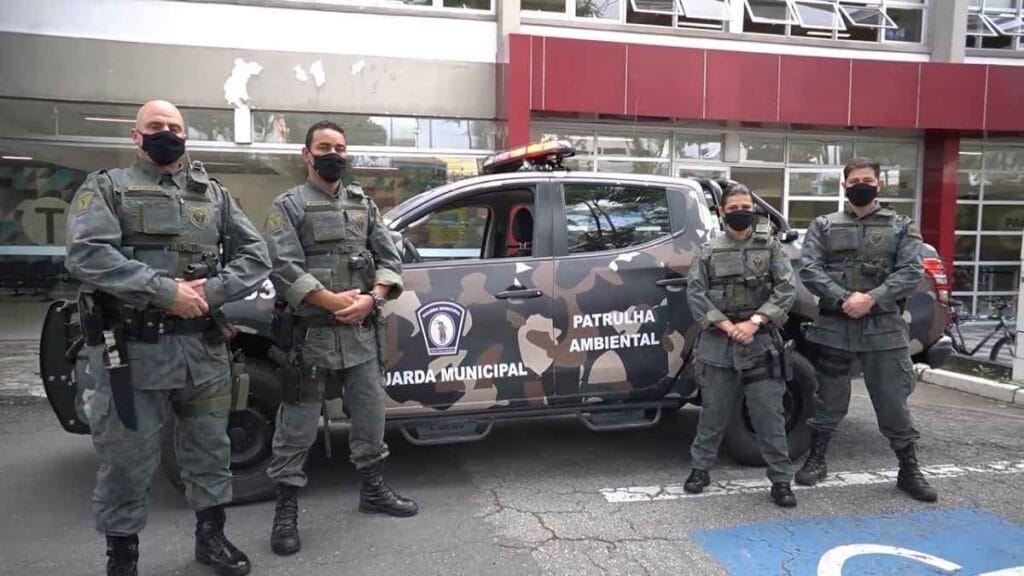 Cinco agentes da Guarda Municipal de Mogi das Cruzes, uniformizados e armados, posam em frente a viatura da Patrulha Ambiental com pintura camuflada.