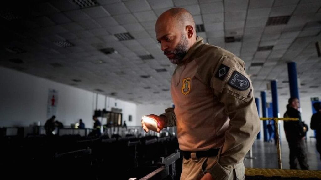 Agente da Guarda Portuária inspeciona área escura com lanterna dentro de terminal no Porto de Santos.