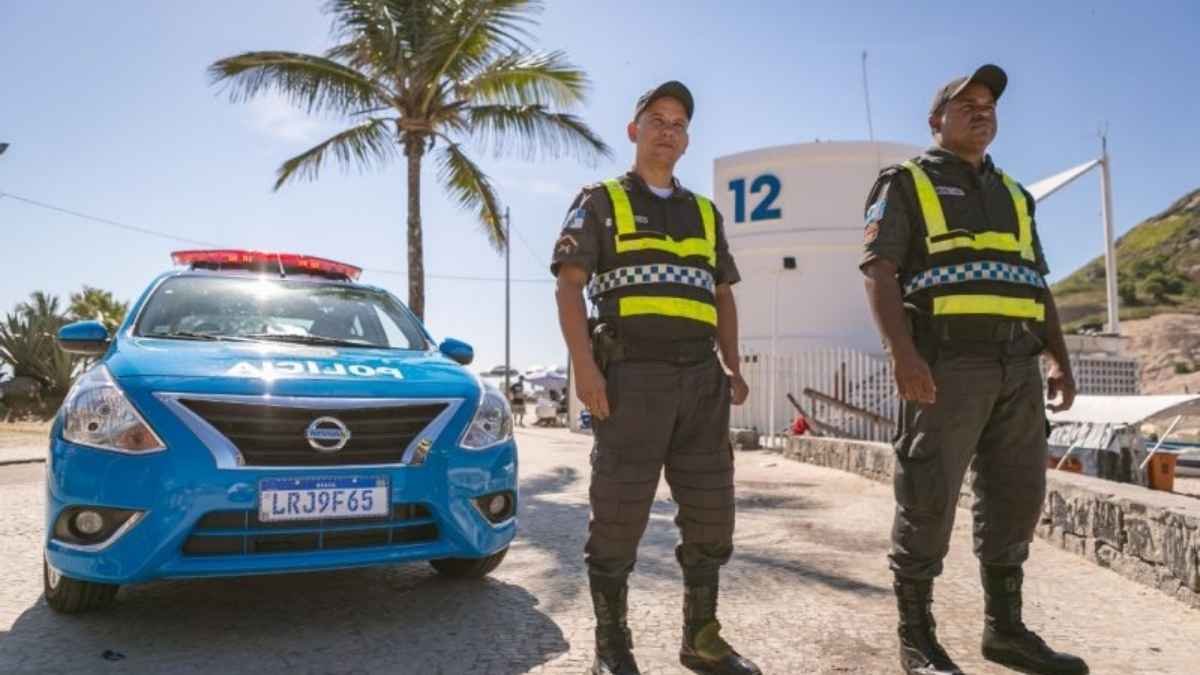 Serviço voluntário: Dois policiais militares do Rio de Janeiro em serviço à beira-mar, ao lado de viatura da PMERJ, usando coletes reflexivos em frente ao posto 12.