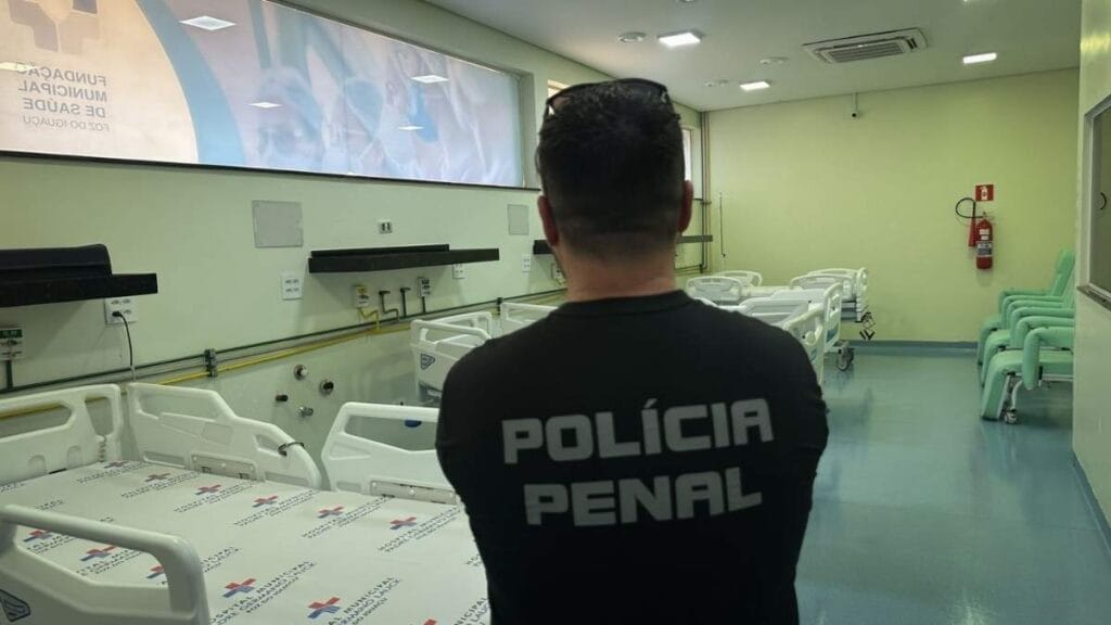 Agente da Polícia Penal observa leitos hospitalares vazios em unidade de saúde pública, durante atividade de custódia de presos.