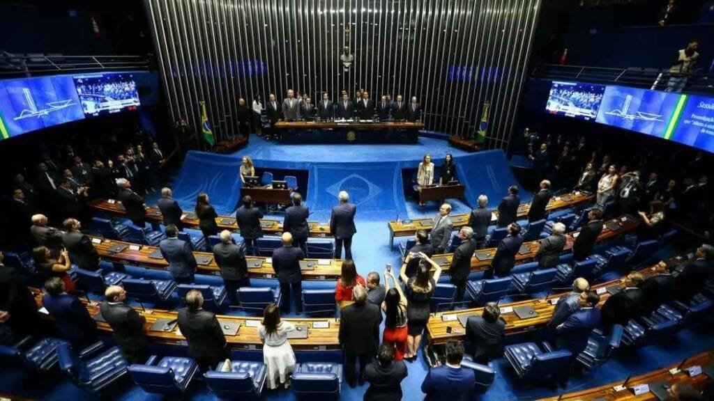 Plenário do Congresso Nacional durante sessão, com parlamentares em pé e autoridades reunidas à mesa diretora.