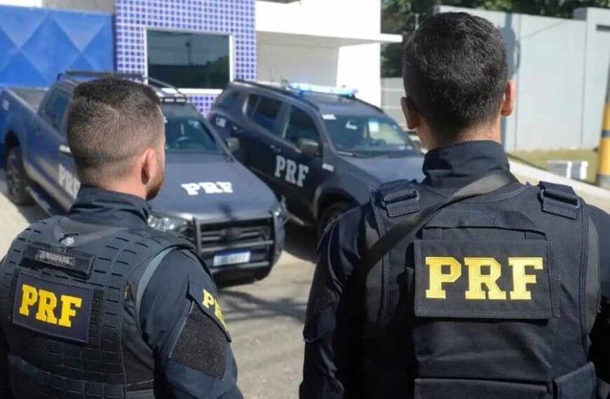 Aposentadoria Policial: Dois policiais da PRF de costas observam viaturas estacionadas em frente a uma unidade da corporação.