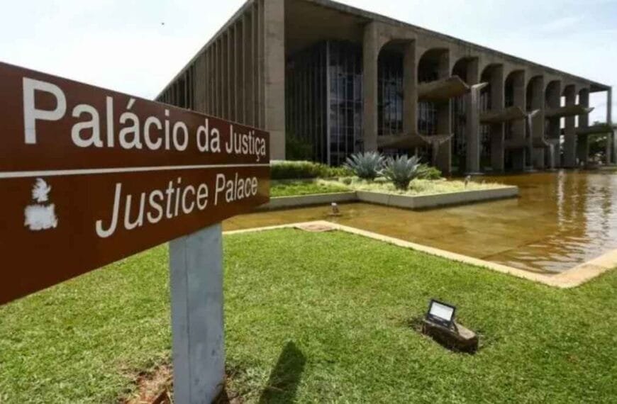 PEC da Segurança empacou? A imagem mostra a fachada do **Palácio da Justiça**, em Brasília, sede do Ministério da Justiça e Segurança Pública. Em primeiro plano, há uma placa marrom com os dizeres “Palácio da Justiça / Justice Palace”. O prédio aparece ao fundo, com arquitetura marcante de colunas e vidraças, ladeado por um espelho d’água e área verde.