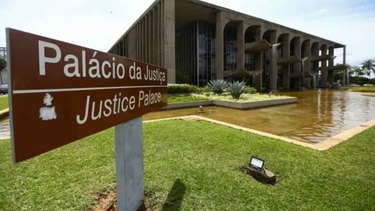 PEC da Segurança empacou? A imagem mostra a fachada do **Palácio da Justiça**, em Brasília, sede do Ministério da Justiça e Segurança Pública. Em primeiro plano, há uma placa marrom com os dizeres “Palácio da Justiça / Justice Palace”. O prédio aparece ao fundo, com arquitetura marcante de colunas e vidraças, ladeado por um espelho d’água e área verde.