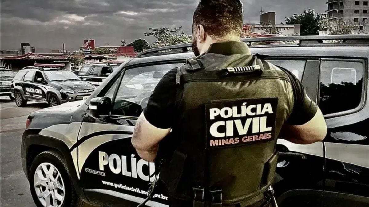 Limite de jornada de 144 horas avança: Policial civil de Minas Gerais, de colete tático com a inscrição “Polícia Civil Minas Gerais”, está em frente a uma viatura oficial preta e branca. Outras viaturas da corporação aparecem estacionadas ao fundo.