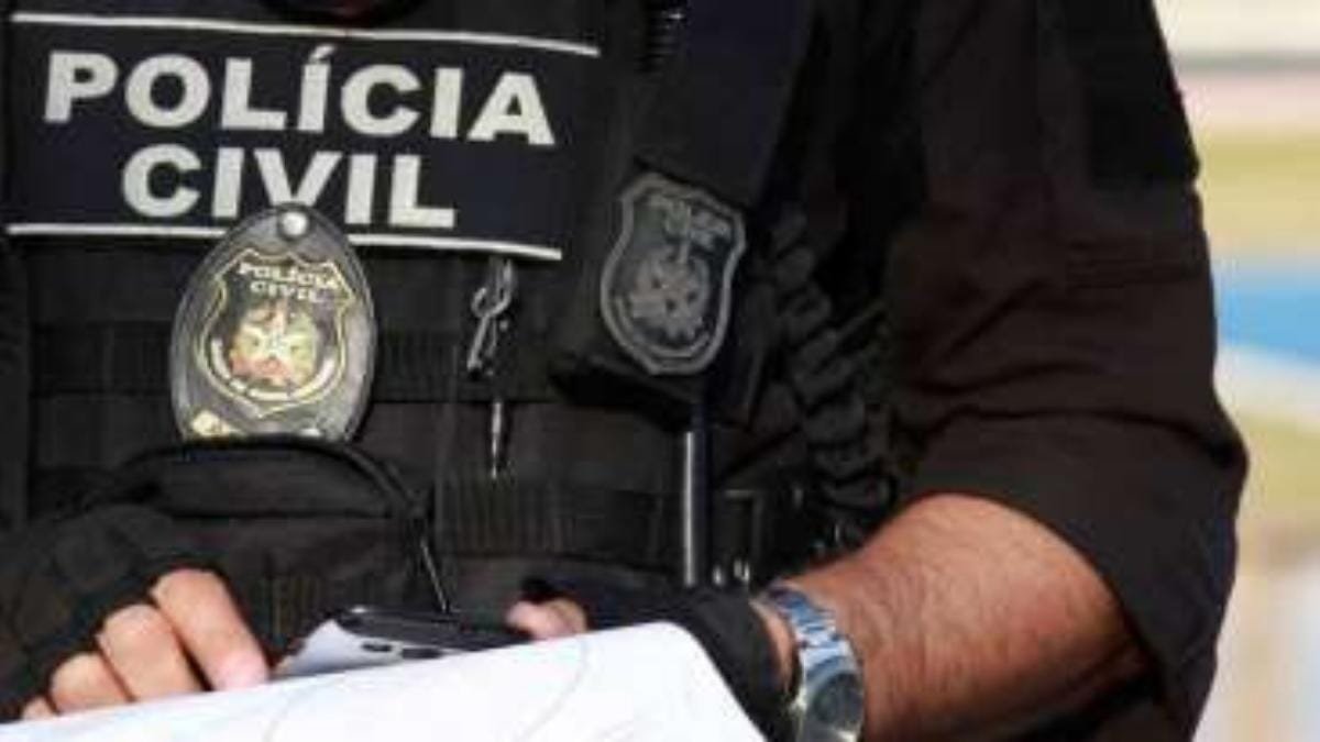 PCAL x Exército: - Um policial civil aparece na imagem usando colete tático preto com a identificação “POLÍCIA CIVIL” e distintivo visível. Ele segura documentos e um celular.