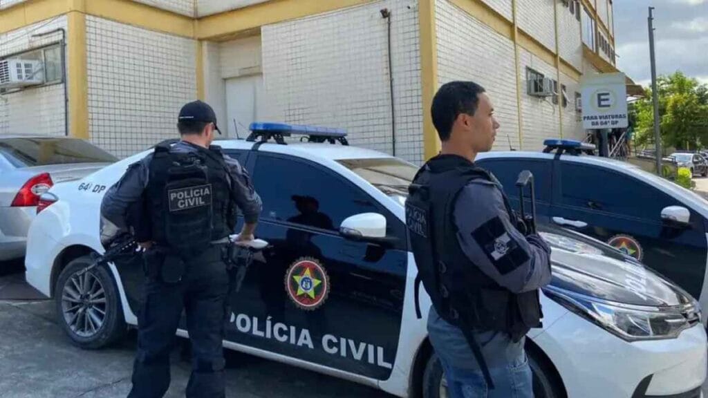 Dois policiais civis armados e fardados estão ao lado de viaturas da Polícia Civil estacionadas em frente a uma delegacia. Ao fundo, há o prédio da delegacia com fachada de azulejos e um letreiro indicando "64ª DP".