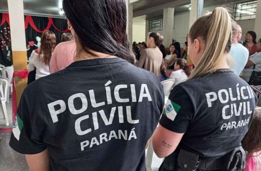 Envelhecimento das Tropas: Duas policiais civis do Paraná, de costas, vestindo camisetas pretas com a inscrição “POLÍCIA CIVIL PARANÁ”. Elas estão em um ambiente interno com outras pessoas ao fundo, em um evento coletivo.