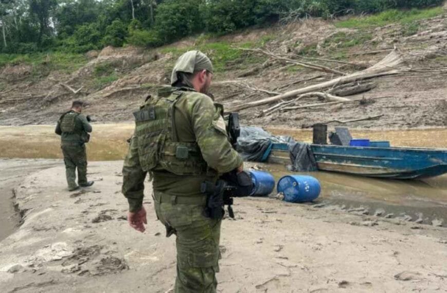 Resumo em texto alt para a matéria: **Texto alt:** Mapa da Amazônia com destaque para áreas em vermelho sob influência do narcotráfico. Ícones representam rotas de drogas, garimpo ilegal e exploração de madeira. Pequenas comunidades indígenas e ribeirinhas aparecem cercadas, simbolizando a ameaça às populações tradicionais.