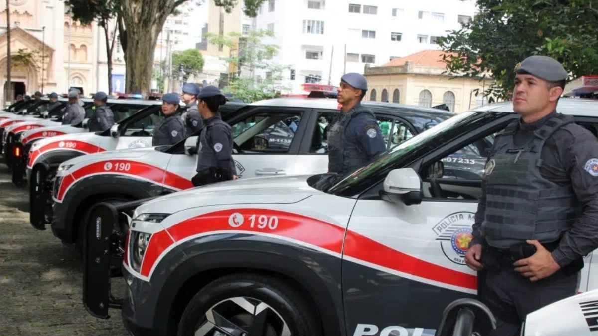 Viaturas da Polícia Militar de São Paulo enfileiradas em área urbana durante cerimônia oficial; policiais fardados estão posicionados ao SUVs: lado dos veículos, que apresentam a pintura tradicional da corporação.