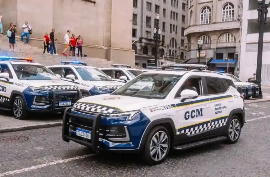 GCM de São Paulo e São Caetano atuam juntas - A imagem mostra viaturas da **Guarda Civil Metropolitana (GCM) de São Paulo**, alinhadas em via pública no centro da cidade, com sirenes ligadas. Os veículos têm pintura branca e azul, com faixas quadriculadas e o brasão da corporação. Ao fundo, pessoas observam próximas a uma escadaria de prédio histórico.