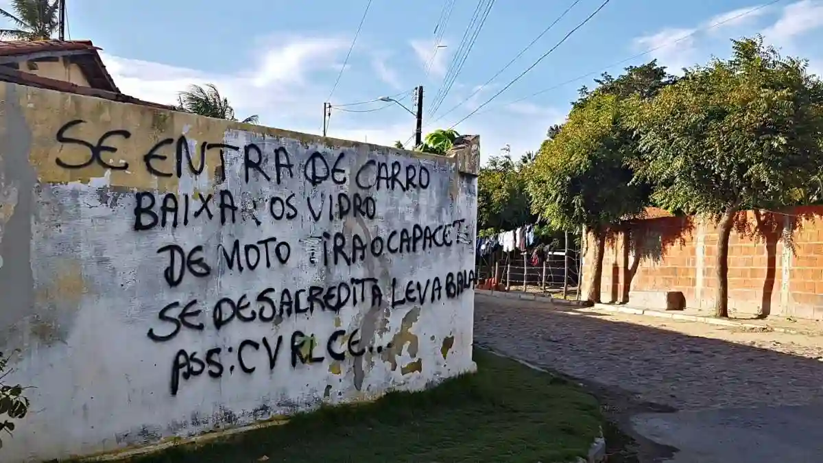 Ceará tomado por facções-O texto escrito no muro da imagem diz: **“Se entra de carro baixa os vidro. De moto tira o capacete. Se desacredita leva bala. Ass: CV RL CE…”** É um recado de facção criminosa impondo regras de circulação em comunidade sob seu domínio.
