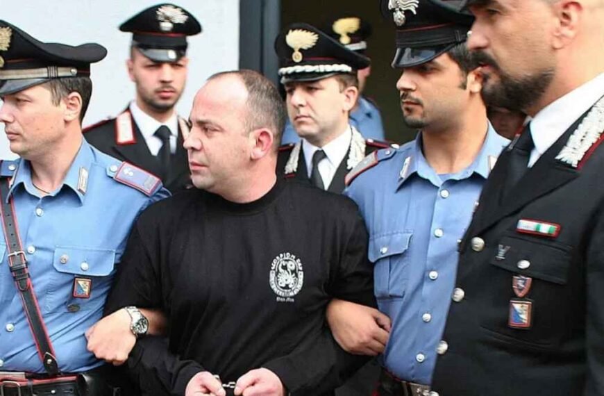 Crime Organizado-Homem algemado é escoltado por vários policiais italianos de uniforme, em operação contra o crime organizado.