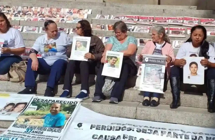 Recorde: 80 mil desaparecidos em 2024-Pessoas sentadas em degraus exibem cartazes com fotos de familiares desaparecidos. À frente, faixas e painéis também mostram imagens e informações de pessoas desaparecidas, em ato de protesto e busca por visibilidade.