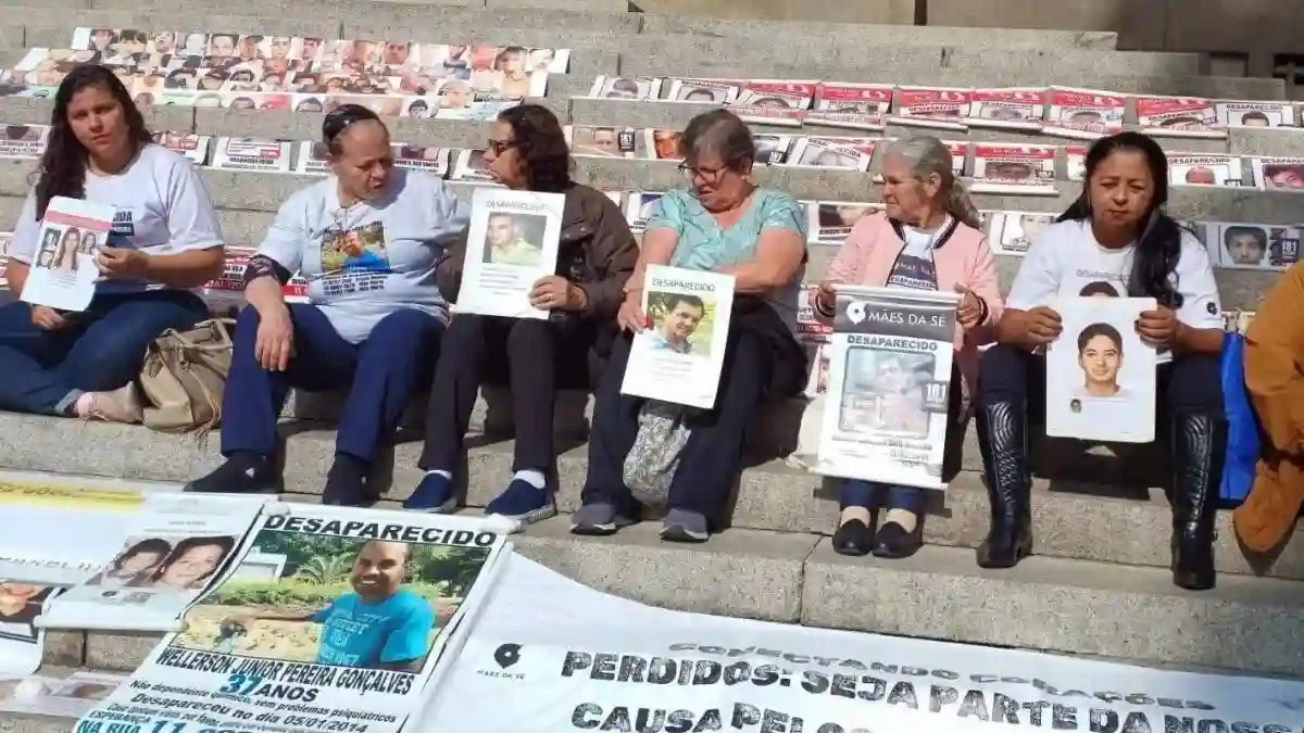 Recorde: 80 mil desaparecidos em 2024-Pessoas sentadas em degraus exibem cartazes com fotos de familiares desaparecidos. À frente, faixas e painéis também mostram imagens e informações de pessoas desaparecidas, em ato de protesto e busca por visibilidade.