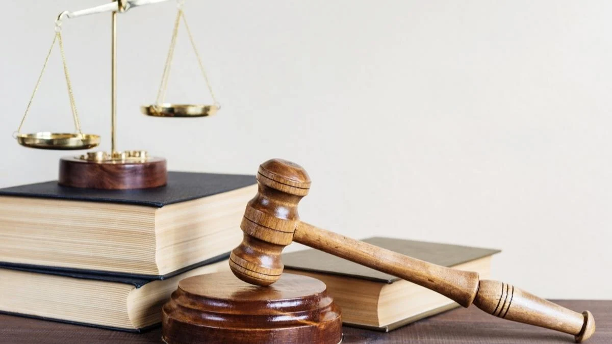 Solto 21 vezes: Martelo de juiz apoiado em base de madeira, ao lado de livros de direito e balança dourada da justiça sobreposta, simbolizando o poder judiciário