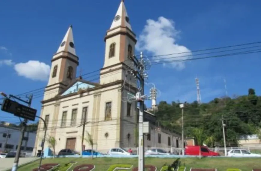 Disfarçados de catadores de latinha - A imagem mostra uma igreja com duas torres em destaque, localizada em uma área urbana com carros estacionados e um letreiro em um canteiro gramado que indica “São Gonçalo”.