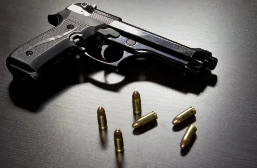 a vingança de um pai - A imagem mostra uma pistola preta apoiada sobre uma superfície escura, ao lado de seis cartuchos de munição dispostos próximos à arma.