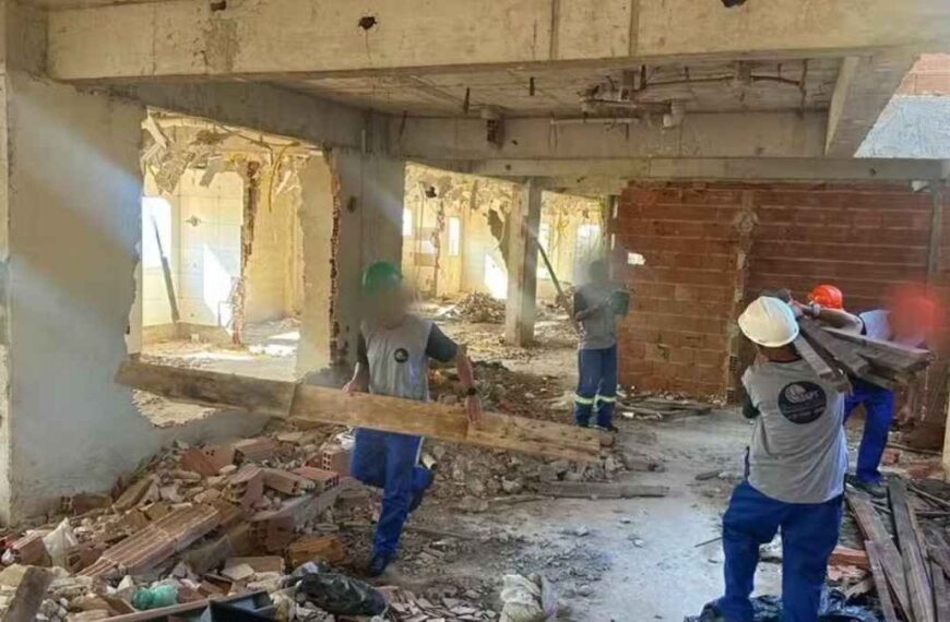 Narcoestado: operários são expulsos de obra pública Trabalhadores com capacetes e equipamentos de proteção realizam demolição e retirada de entulhos em prédio em obras.