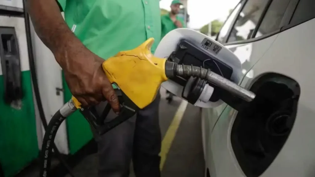 Frentista abastece carro branco com bomba de combustível de bico amarelo.