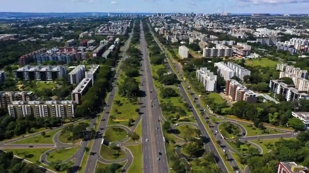 Vista aérea do Eixo Rodoviário em Brasília, com largas avenidas paralelas cercadas por áreas verdes e blocos residenciais.