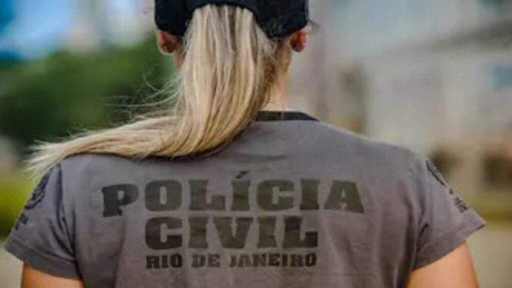 Promoção na PCRJ geram insatisfação -Policial civil do Rio de Janeiro, vista de costas, usa camiseta com a inscrição "Polícia Civil Rio de Janeiro" e boné preto, com cabelo preso em rabo de cavalo.
