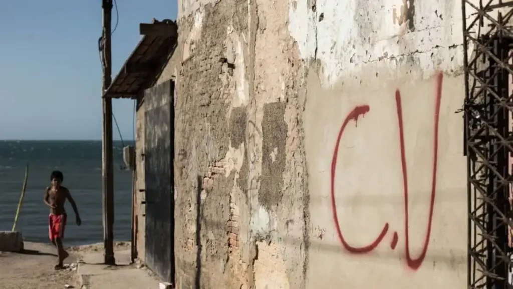 A imagem mostra uma parede deteriorada com a pichação “C.V” em vermelho, sigla associada a facção criminosa.