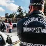 Leniência judicial impede combate ao crime pela GCM-Agente da Guarda Civil Metropolitana, de costas, próximo a uma viatura, acompanha ação em área urbana com outras pessoas e policiais ao fundo.