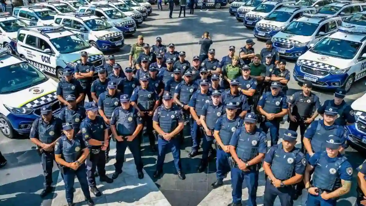 Universidade da GCM-SP-Grupo de guardas civis municipais em formação, posicionados em frente a diversas viaturas oficiais estacionadas lado a lado.