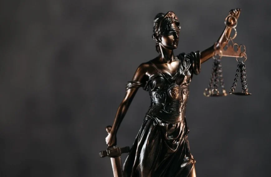 A imagem mostra uma estátua de bronze da deusa da Justiça, com os olhos vendados, segurando uma balança em uma das mãos e uma espada na outra.