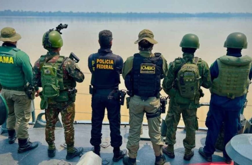 Garimpo ilegal: PF enxuga gelo? Agentes do Ibama, Exército, Polícia Federal e ICMBio, equipados com fardas e coletes, observam rio durante operação conjunta contra o garimpo ilegal na Amazônia.