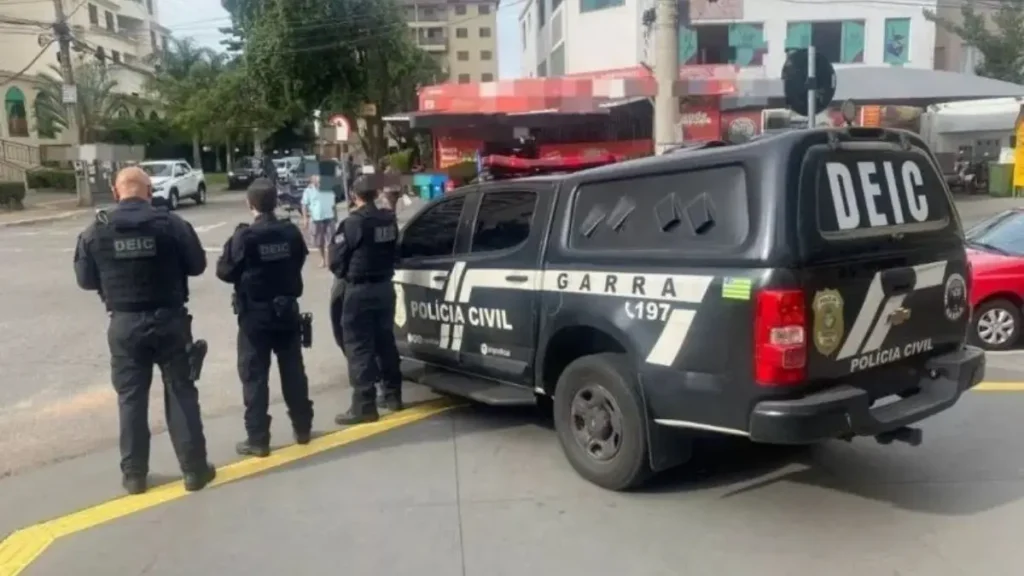A imagem mostra policiais civis do **DEIC** em pé ao lado de uma viatura preta identificada com as inscrições **“POLÍCIA CIVIL”**, **“DEIC”** e **“GARRA”**, estacionada em uma rua de área urbana.
