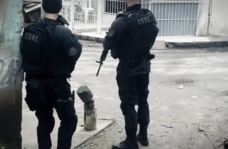 PCERJ terá gratificação de até 150%-Dois policiais civis do CORE (Coordenadoria de Recursos Especiais) aparecem de costas, armados e equipados com coletes táticos, em uma rua de comunidade, durante operação.