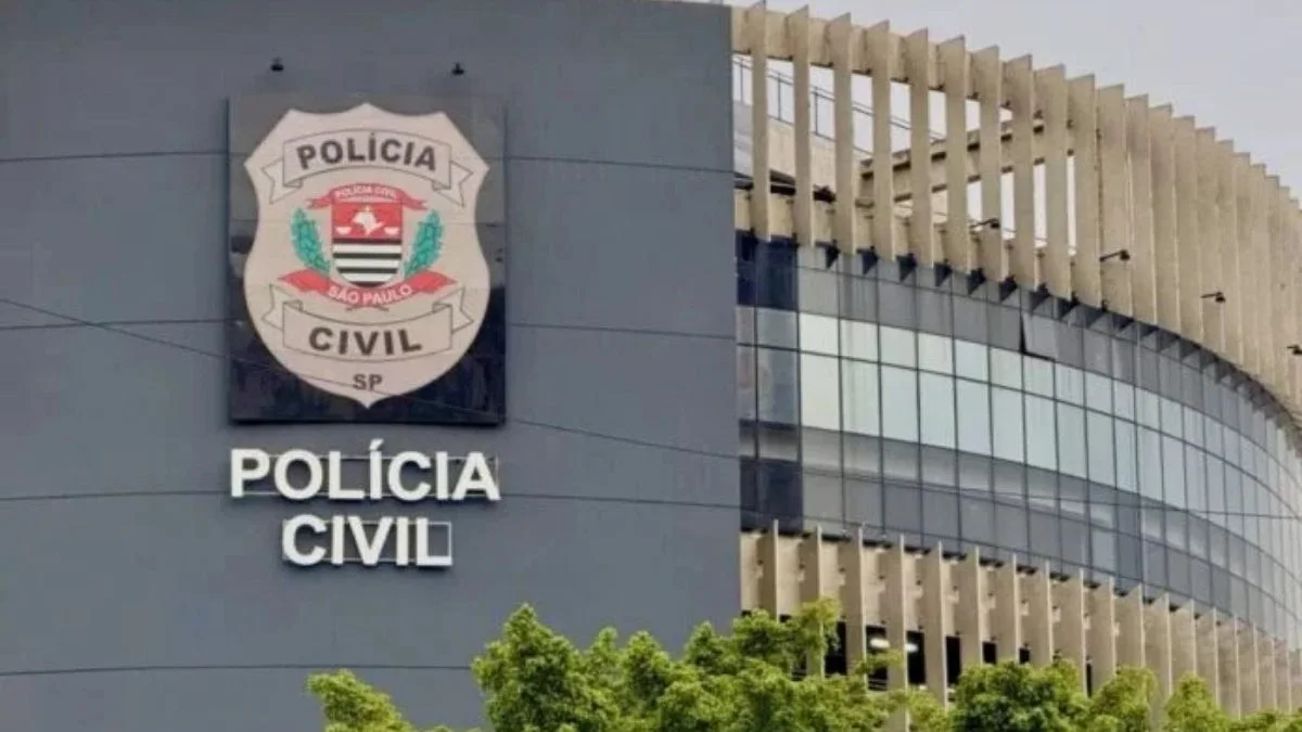 SP: Lei Orgânica da PC não avança-A imagem mostra a fachada de um prédio da Polícia Civil de São Paulo, com o brasão oficial da corporação em destaque na parede, acompanhado da inscrição "Polícia Civil". A construção tem design moderno, com vidros espelhados e elementos arquitetônicos verticais na parte externa.
