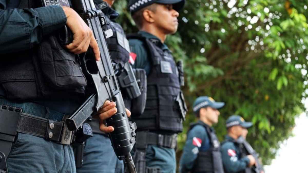 Quem lembra dos municípios na segurança pública? A imagem mostra policiais fardados em formação, usando coletes táticos e armamento pesado, em ambiente externo com árvores ao fundo.