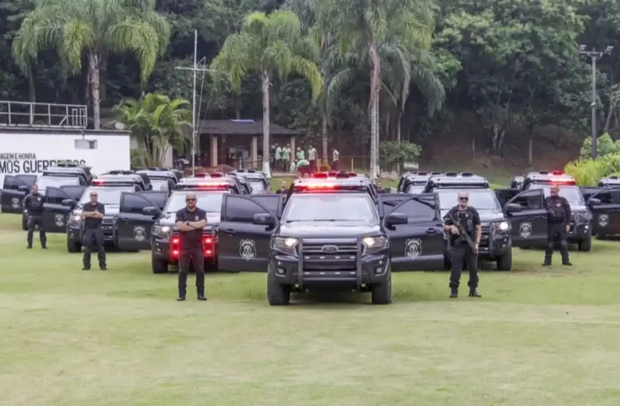 Reestruturação da PPRJ não avança-Policiais penais aparecem perfilados ao lado de viaturas pretas com sirenes ligadas, em área gramada com árvores ao fundo, em formação de exibição operacional.