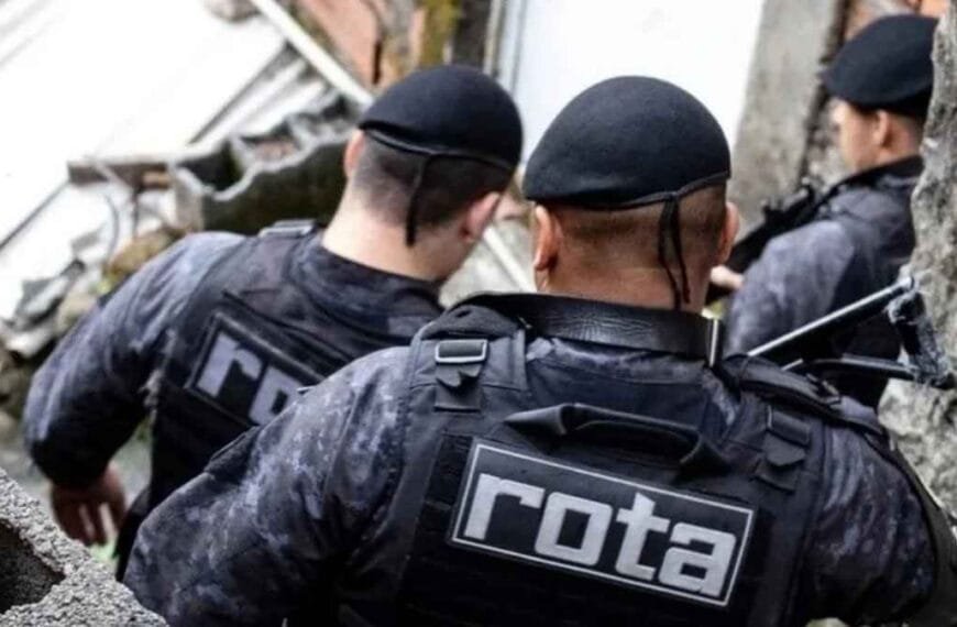 Operação Escudo: Policiais militares da ROTA, unidade de elite da PM de São Paulo, em operação em área urbana, circulando por vielas estreitas com equipamentos táticos e coletes identificados.