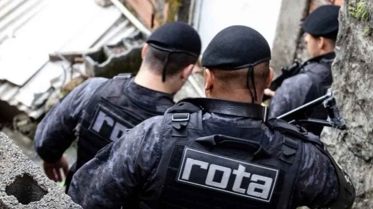 Operação Escudo: Policiais militares da ROTA, unidade de elite da PM de São Paulo, em operação em área urbana, circulando por vielas estreitas com equipamentos táticos e coletes identificados.
