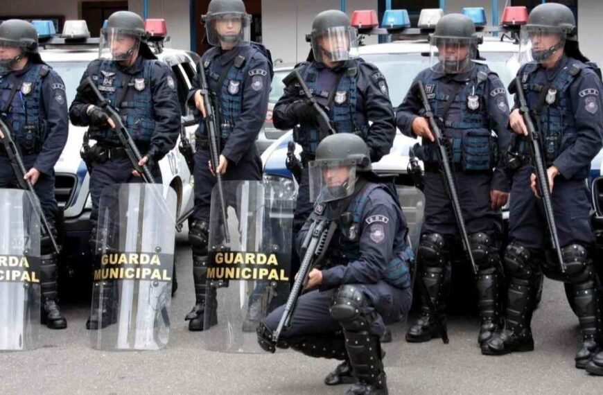 formação de choque, equipados com escudos, capacetes e armas não letais, prontos para atuação em controle de distúrbios civis.