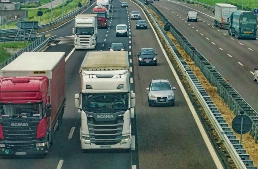 O crime na cadeia de suprimento-Rodovia com tráfego intenso, mostrando caminhões e carros em várias faixas, separados por barreiras de proteção.