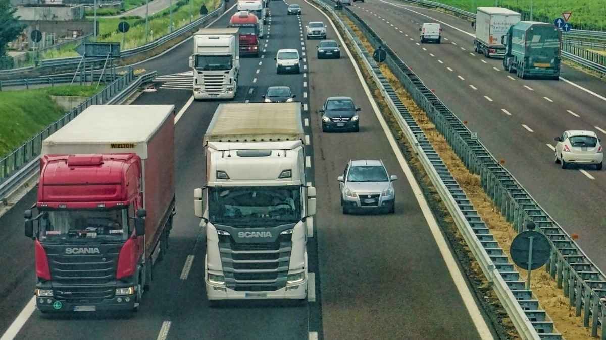 O crime na cadeia de suprimento-Rodovia com tráfego intenso, mostrando caminhões e carros em várias faixas, separados por barreiras de proteção.