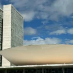 Vista do Congresso Nacional em Brasília, com as torres gêmeas e a cúpula branca em destaque sob o céu azul com nuvens