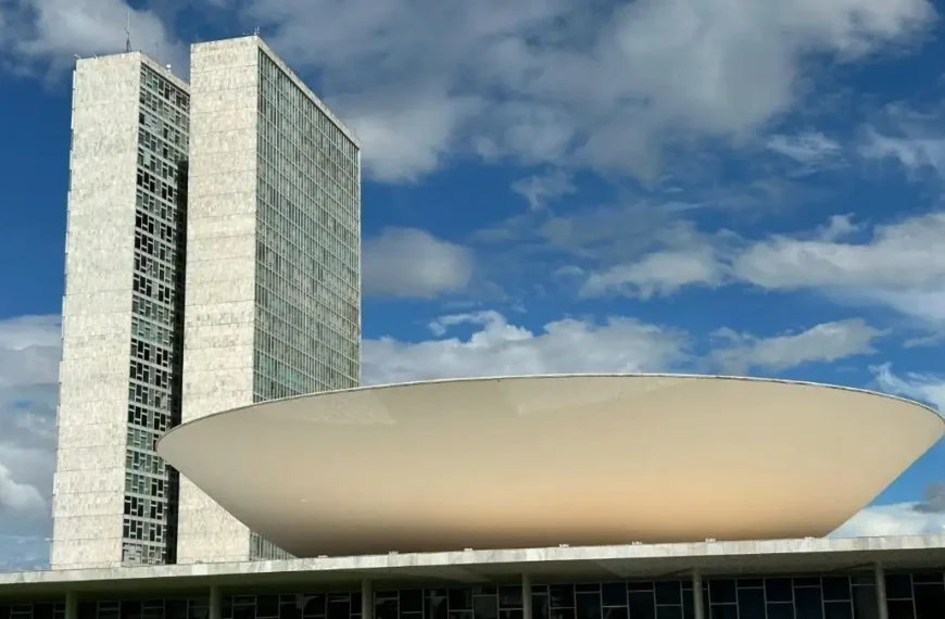Vista do Congresso Nacional em Brasília, com as torres gêmeas e a cúpula branca em destaque sob o céu azul com nuvens
