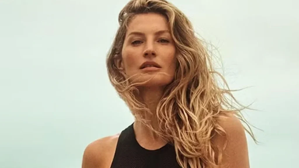 Mulher loira de cabelos ondulados usa roupa esportiva preta em ambiente externo com céu nublado ao fundo